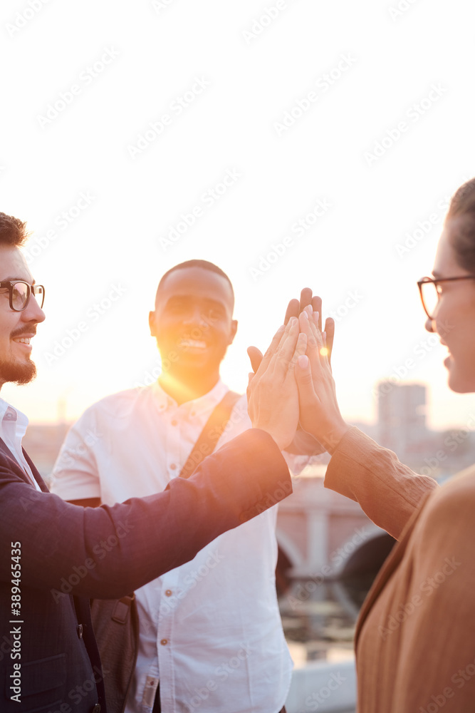 Poster cheerful colleagues giving each other high five while standing by riverside