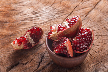 slices of pomegranate on an old wooden background, pomegranate in a clay bowl, slice of pomegranate on a wooden background
