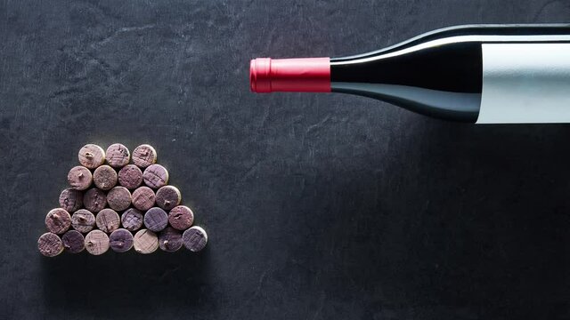 Wine corks shaped Christmas tree on black background with a bottle of red wine. Stop motion, timelapse. Copy space.