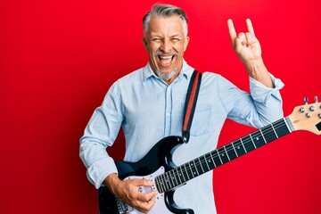 Middle age grey-haired man playing electric guitar doing rock sign smiling and laughing hard out loud because funny crazy joke.