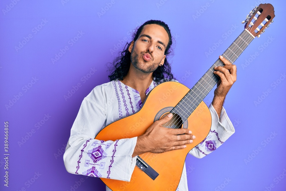 Sticker young handsome man with long hair playing classical guitar looking at the camera blowing a kiss bein