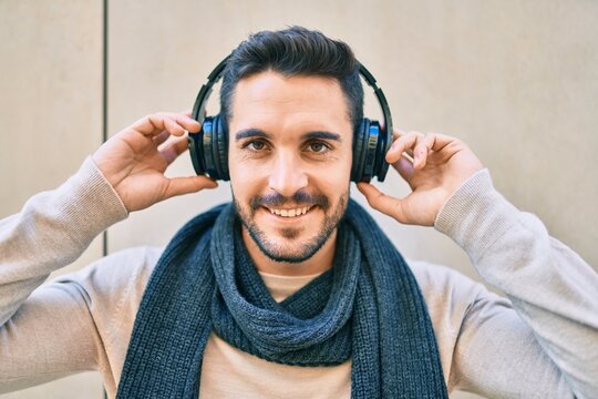 Young hispanic man smiling happy listening to music using headphones at the city.