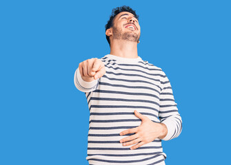 Fototapeta premium Young hispanic man wearing casual clothes laughing at you, pointing finger to the camera with hand over body, shame expression