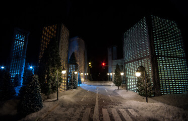 Fototapeta na wymiar Little miniature city with road and lights. Decorative cute small houses in snow at night in winter. Creative Holiday concept. Christmas and New Year attributes decorated composition.