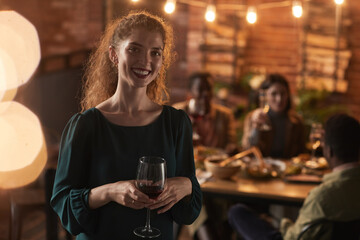 Waist up portrait of smiling young woman holding champagne glass and looking at camera while enjoying party outdoors, copy space