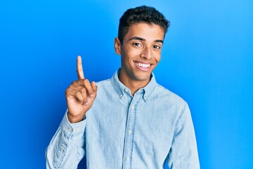 Young handsome african american man wearing casual clothes smiling with an idea or question pointing finger up with happy face, number one
