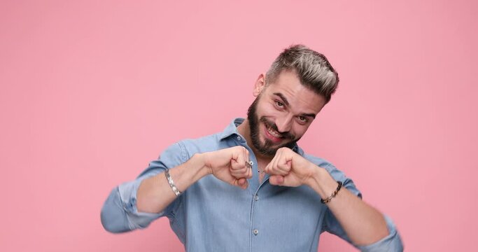 young casual guy rubbing his palms and smirking then clapping his fists and his hands against pink background