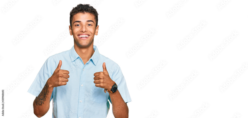 Wall mural Young handsome african american man wearing casual clothes success sign doing positive gesture with hand, thumbs up smiling and happy. cheerful expression and winner gesture.