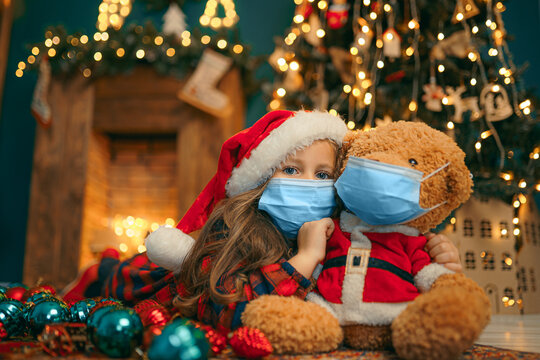 Portrait of cutel little child girl in medical mask playing with Taddy bear, New year holiday concept. Covid-19 concept.