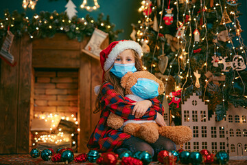 Portrait of cutel little child girl in medical mask playing with Taddy bear, New year holiday concept. Covid-19 concept.