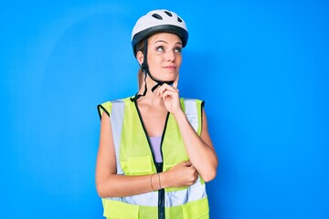 Young caucasian girl wearing bike helmet and reflective vest serious face thinking about question with hand on chin, thoughtful about confusing idea