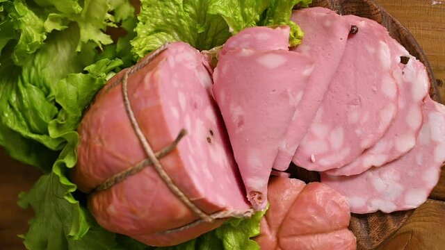  Italian Whole block of mortadella on a wooden plate. Traditional big sausage and black pepper pistachios Region Emilia Romagna and the city of Bologna. Top view. Vertical footage