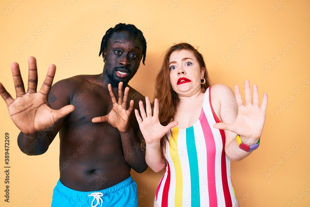 Poster interracial couple wearing swimwear afraid and terrified with fear expression stop gesture with hand