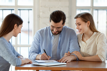 Becoming owners. Happy satisfied young couple husband and wife signing up paper documents,...