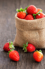 Fresh ripe harvested strawberries in burlap sack on wooden table, Garden summer fruit, strawberry, copy space ( Fragaria )