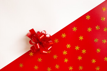 Red plastic bow on a red and white diagonal paper texture with golden snowflakes
