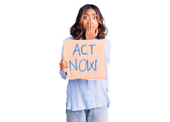 Young beautiful mixed race woman holding act now banner covering mouth with hand, shocked and...