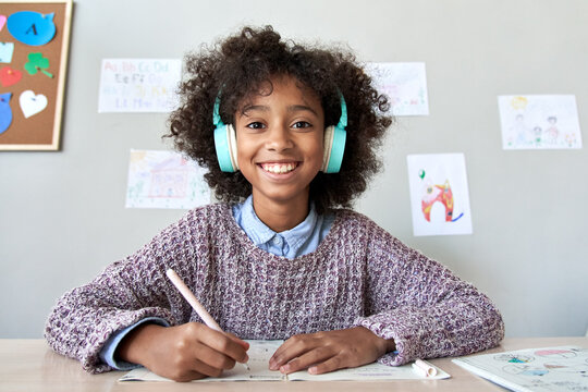 Happy african american kid child girl wearing headphones looking at web cam talking with remote teacher on distance learning video conference call chat class, headshot zoom portrait, webcam view.