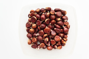 Top view of raw chestnuts on container on white background