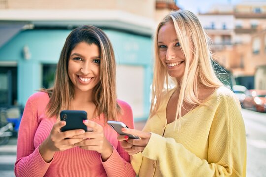 Two beautiful and young girl friends together having fun at the city using smartphone