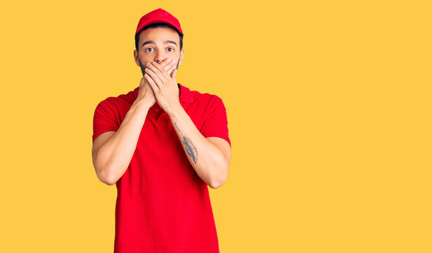 Young handsome hispanic man wearing delivery courier uniform shocked covering mouth with hands for mistake. secret concept.