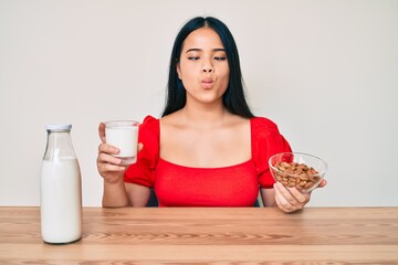 Young asian girl drinking healthy almond milk making fish face with mouth and squinting eyes, crazy and comical.