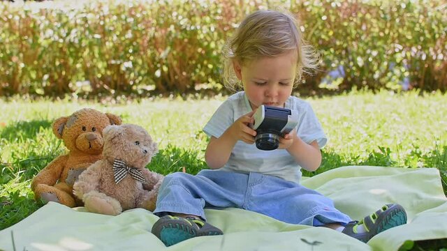 Cute little child holding a vintage film camera and taking photo of his teddy bear