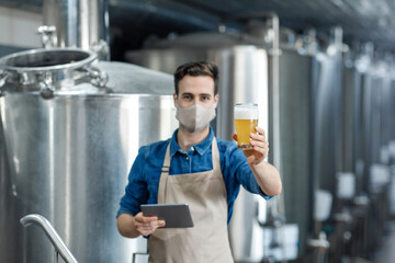 Confident specialist in apron holds beer glass, brewery expert controlling quality of ale