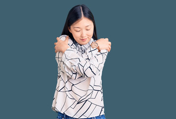 Young beautiful chinese woman wearing casual shirt hugging oneself happy and positive, smiling...