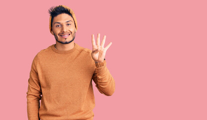 Handsome latin american young man wearing winter sweater and wool hat showing and pointing up with fingers number four while smiling confident and happy.