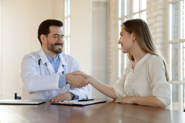 Thank you for help, doctor. Happy grateful young woman patient handshaking with male physician appreciating for good effect of treatment, satisfied with better health state, signing insurance policy