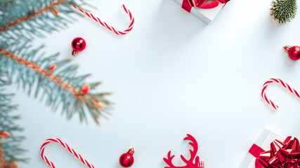 Holiday winter background. White gift box with red ribbon, New Year balls and sparkling lights in Christmas composition on white for greeting card. Flat lay, top view, copy space.