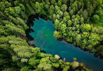 Aerial view of a turquoise pond in the middle of a forest in Finland