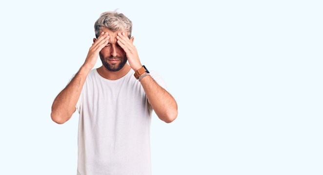 Young handsome blond man wearing casual t-shirt with hand on head for pain in head because stress. suffering migraine.