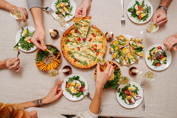 Overhead view of hands of dining people over table with Italian cuisine assorti.