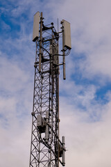 Tower with 5G and 4G cellular network antenna on blue cloudy sky background.