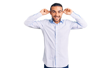 Young handsome man wearing business clothes smiling pulling ears with fingers, funny gesture....