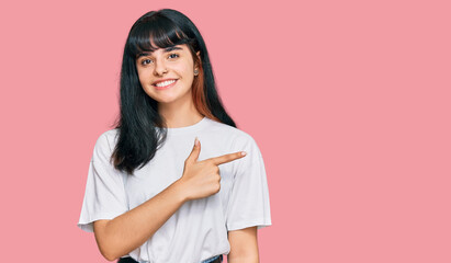 Fototapeta premium Young hispanic girl wearing casual clothes cheerful with a smile of face pointing with hand and finger up to the side with happy and natural expression on face