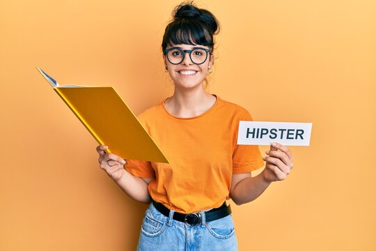 Young hispanic girl reading book and holding paper with hipster message smiling with a happy and cool smile on face. showing teeth.