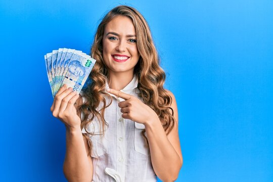 Young blonde girl holding south african 20 rand banknotes smiling happy pointing with hand and finger