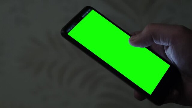 Smartphone with green screen in man's hand. Close-up mobile phone with blank screen.