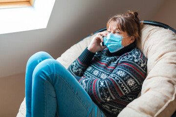 The woman is in self isolation in the house. The woman is very emotionally talking on the phone sitting in a chair.