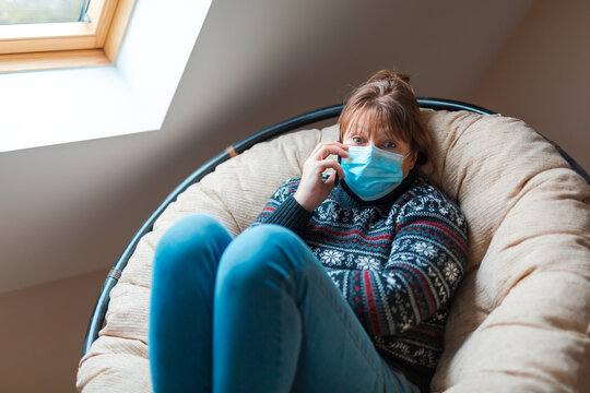 The woman is in self isolation in the house. The woman is very emotionally talking on the phone sitting in a chair.