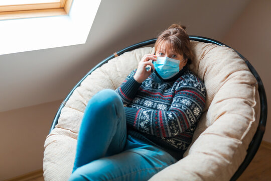 The woman is in self isolation in the house. The woman is very emotionally talking on the phone sitting in a chair. - Powered by Adobe