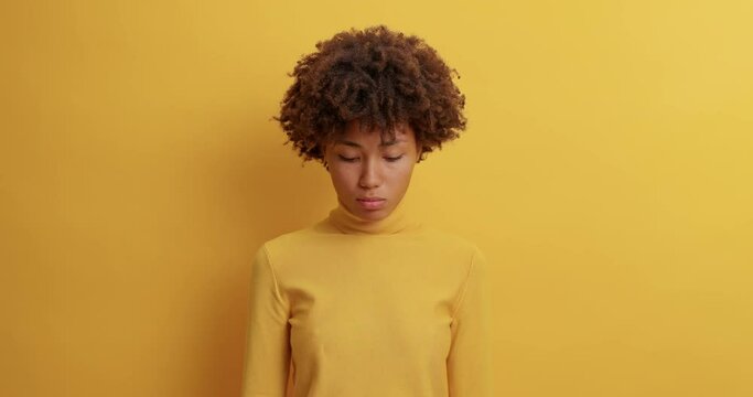 Disappointed sad woman has melancholic look at camera purses lips being offended has hurt feelings feels lonely dressed in casual wear poses against yellow background. Negative emotions concept