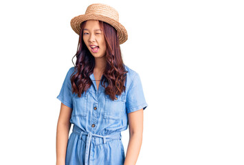 Young beautiful chinese girl wearing summer hat winking looking at the camera with sexy expression,...
