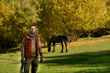 Fototapeta premium A black horse and a a man on a sunny autumn day.