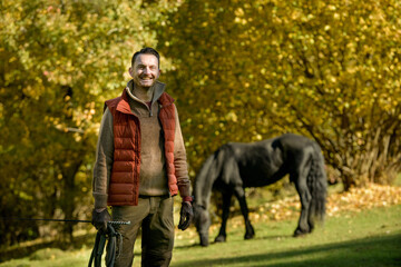 Fototapeta premium A black horse and a a man on a sunny autumn day.