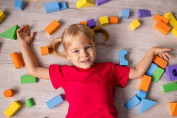 Happy preschool girl playing with colorful plastic toy cubes. Top view from above.
