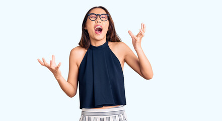 Young beautiful chinese girl wearing casual clothes and glasses crazy and mad shouting and yelling with aggressive expression and arms raised. frustration concept.